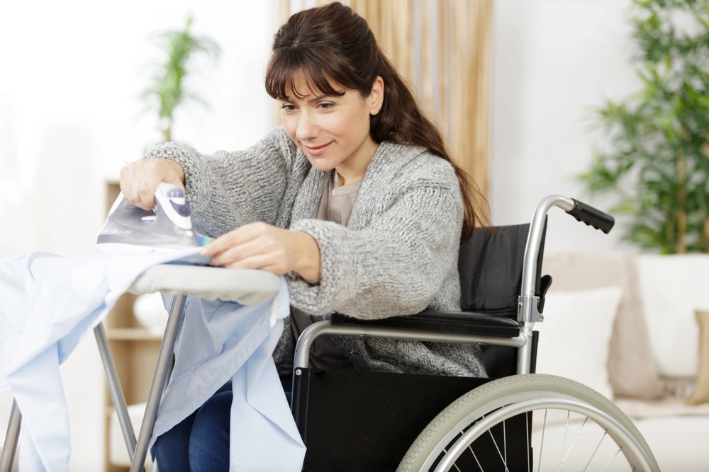 women on wheel chair pressing and ironing clothes in her home
