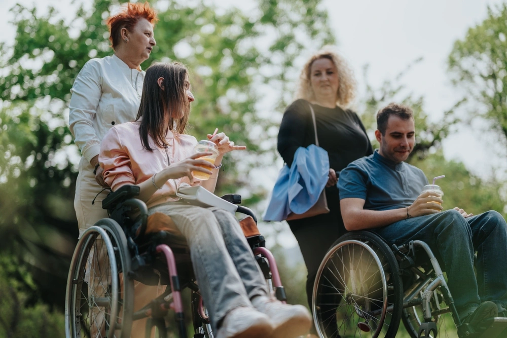 two disabled individuals with carers in a park